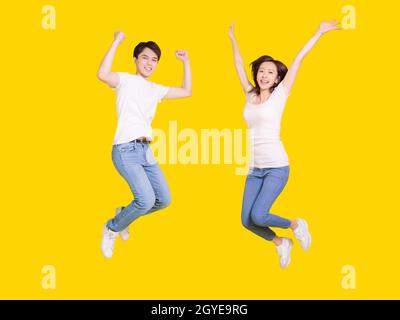 Happy couple jumping.Young man and woman having fun together.Isolated over yellow background. Stock Photo