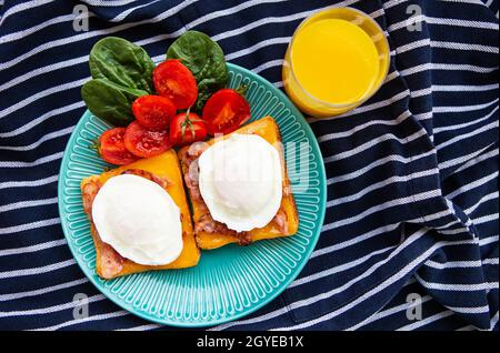 Poached egg on toasted English toast with spinach, cherry tomatoes, orange juice, striped napkin. Stock Photo