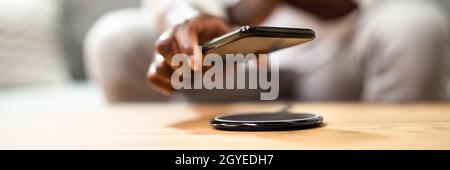 Man Charging Smartphone Using Wireless Charging Pad At Home Stock Photo