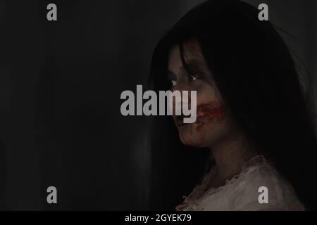 Female zombie in blood. Closeup face and eyes of Asian Woman ghost with blood. Horror creepy scary fear in a dark house. Hair covering the face, Hallo Stock Photo