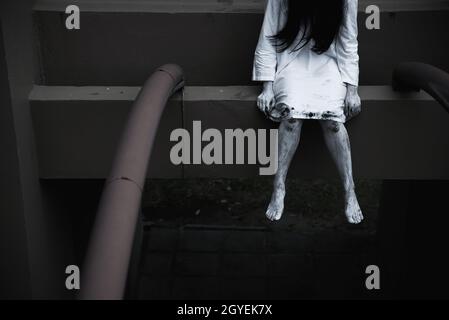 Horror woman ghost creepy sitting hanging legs on building, halloween day concept Stock Photo