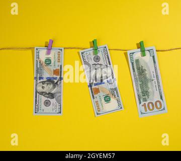 one hundred US dollar bills hang on a rope with clothespins, yellow background. Money laundering concept Stock Photo
