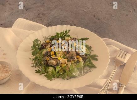 On the table on a plate is an appetizing salad of mushrooms, onions, canned corn and cucumbers. Front view, copy space Stock Photo