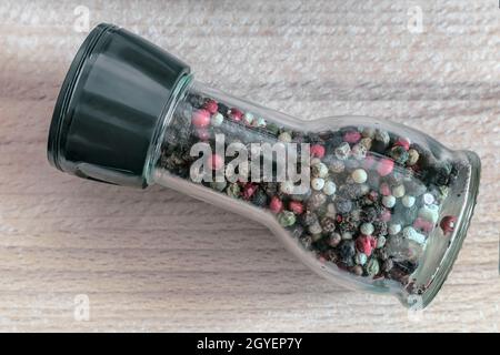 A set of spices: black, white, red pepper peas in a glass bottle on a wooden table. Front view, copy space Stock Photo