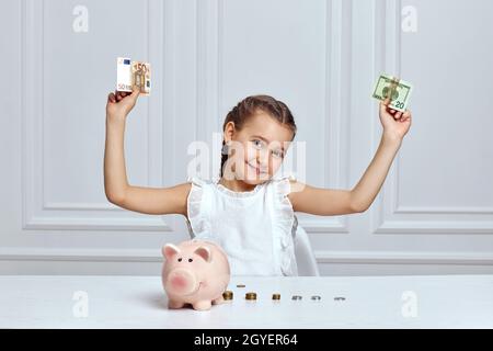 happy cute little girl saving money in pink piggy bank. Stock Photo