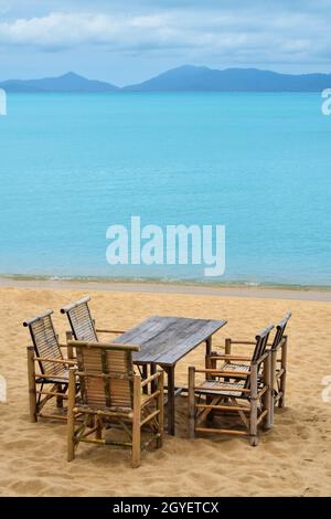 Wooden bamboo furniture, table and five chairs around on sand beach with blue sea water background in Koh Samui island, Thailand Stock Photo