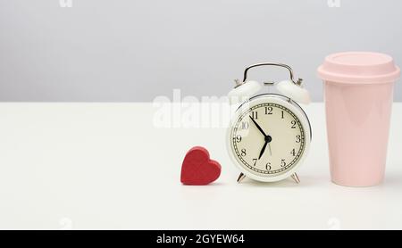 round retro alarm clock and pink ceramic cup with coffee on white table, copy space Stock Photo