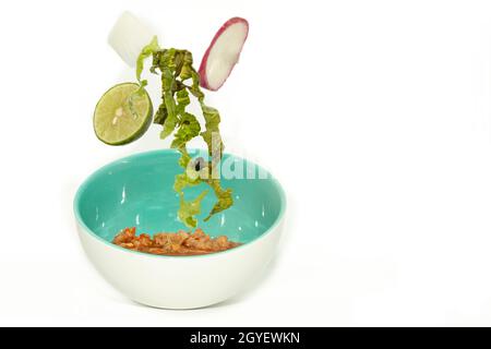 Ingredients falling to the plate, lettuce, radish, lemon onion soup stew pozole typical traditional Mexican food with Corn and Meat served in a Bowl i Stock Photo