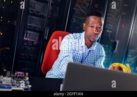 African american male computer technician using laptop working in server room Stock Photo