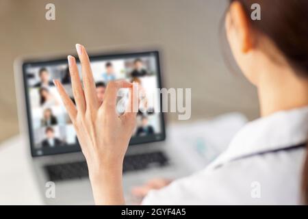 Back view of doctor making video call with laptop and showing ok gesture. Stock Photo