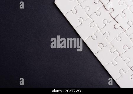 Top view flat lay of paper plain white jigsaw puzzle game texture on a black background, quiz calculation concept Stock Photo