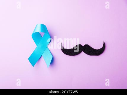 Black mustache paper and light blue ribbon, studio shot isolated on purple background, Prostate cancer awareness month, Fathers day, minimal November Stock Photo