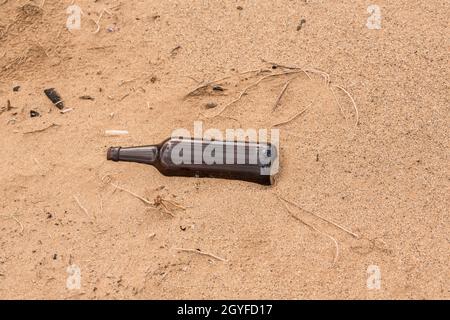 Someone left an empty bottle on the sand instead of recycled it. Stock Photo