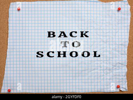 torn crumpled white sheet of paper in a cage pinned to a brown corkboard, lettering back to school Stock Photo
