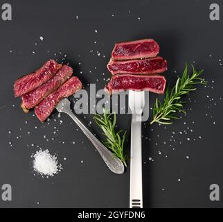 Fried pieces of beef on an iron fork on a black background. The degree of readiness is rare. View from above Stock Photo