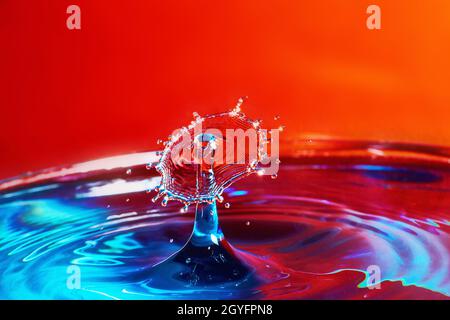 Two water drops colliding on blue water with red background Stock Photo