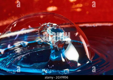 Bubble on blue water surface with two water drops colliding in air on red background Stock Photo
