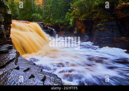 Wet rock path with giant golden and brown waterfall in a deep green forest Stock Photo