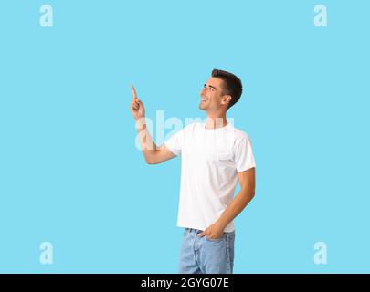 Handsome young man in stylish t-shirt pointing at something on color background Stock Photo