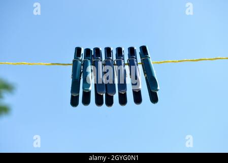 Plastic clothespins hanging on rope against blue sky Stock Photo
