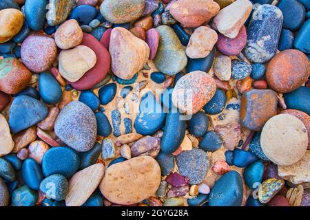 Smooth multicolored stones against a sandy beach Stock Photo
