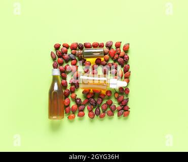 Bottles of essential oil and dried rose hip berries on green background Stock Photo