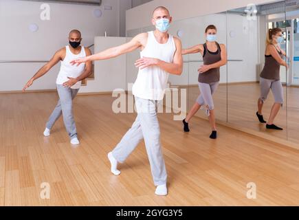 People in protective masks practicing active dance in studio Stock Photo