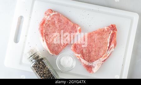 Raw pork chops with salt and black pepper close up on cutting board, flat lay Stock Photo