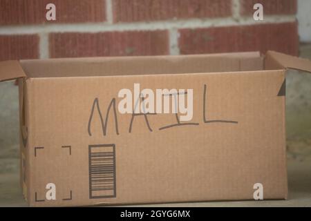 Cardboard box with the word MAIL written on it in front of a red brick house Stock Photo