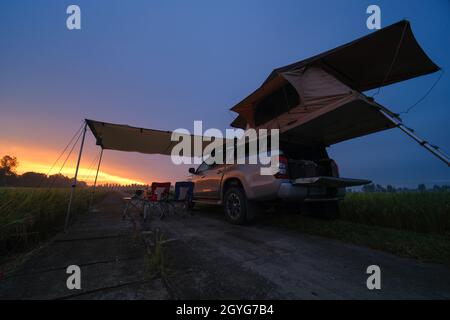 Truck with Roof Top Tent in Field.  Traveling by Car and Camping with rooftop tent. Morning landscape with beautiful sunrise sky. Camp table and chair Stock Photo