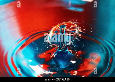 Blue and red water with ripples and splash from two water drops hitting in air Stock Photo