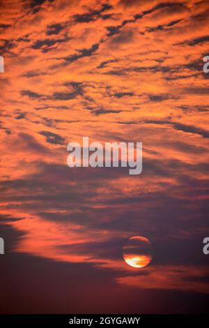 Sun setting in orange sky with clouds Stock Photo