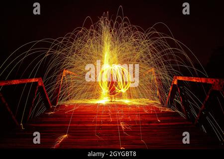 An intertwining circle of yellow light and sparks around a person at night on a bridge Stock Photo