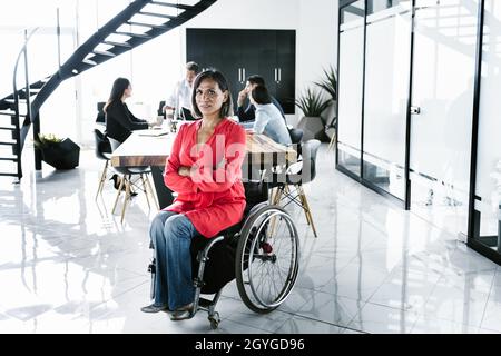 Portrait of latin transgender woman in wheelchair and people at meeting in the background in the office in Latin America Stock Photo