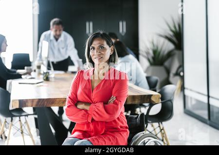 Portrait of hispanic transgender woman sitting on wheelchair with arms crossed in the office in Latin America Stock Photo