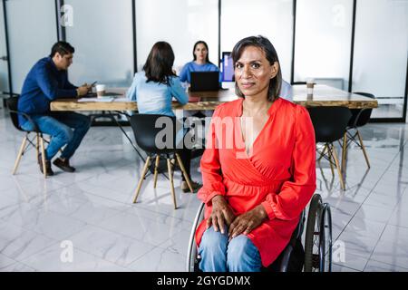 Disabled latina transgender woman in wheelchair at work in conference room In Mexico City Stock Photo
