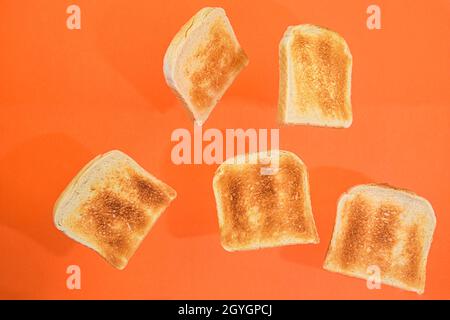Flying roasted pieces of bread on orange pastel background. Fresh roasted pieces of toasts on orange background Stock Photo