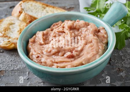 High angle closeup of bowl with appetizing vegetarian pate made of beans served on table with bread slices and parsley sprig Stock Photo