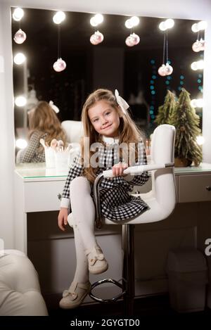 Beautiful little girl with curly hair in a beauty salon against the background of a large mirror. Stock Photo