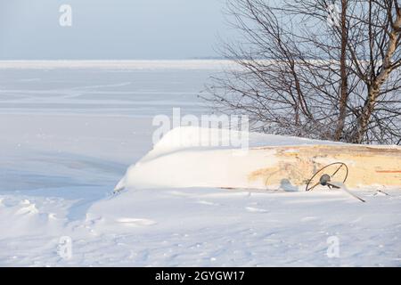 Winter landscape. Small boat lays upside down on white snow on frozen Baltic Sea under blue sky on a sunny day Stock Photo