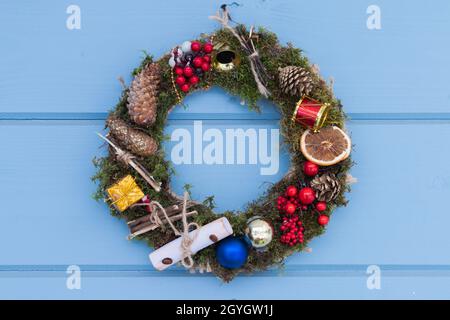 Christmas wreath made of spruce branches with decoration hangs on a blue wooden wall Stock Photo