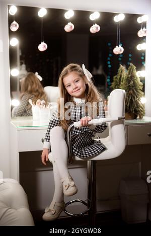 Beautiful little girl with curly hair in a beauty salon against the background of a large mirror. Stock Photo