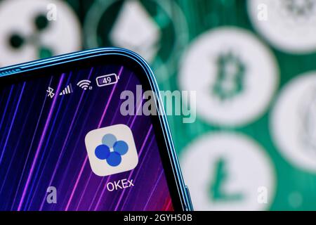 OKEx is a cryptocurrency exchange. OKEx app on smartphone screen against the background of the main cryptocurrencies. Stock Photo