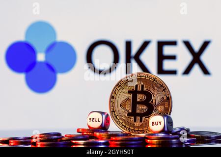 OKEx is a cryptocurrency exchange. Golden bitcoin with two buy-sell cubes in a pile of coins on the background of the OKEx logo. Stock Photo