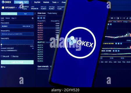 OKEx is a cryptocurrency exchange. A smartphone with the OKEx logo on the background of the live trading webpage. OKEx dashboard. Stock Photo