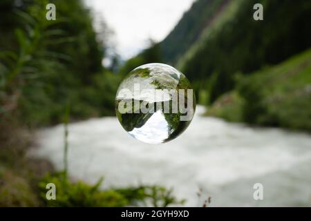 Glass sphere floating over river in the alps, cloudy day in summer Stock Photo