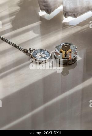 A retro pocket watch and Old vintage iron padlock is placed on the floor of the room that have early light through the beautiful curtain for backgroun Stock Photo