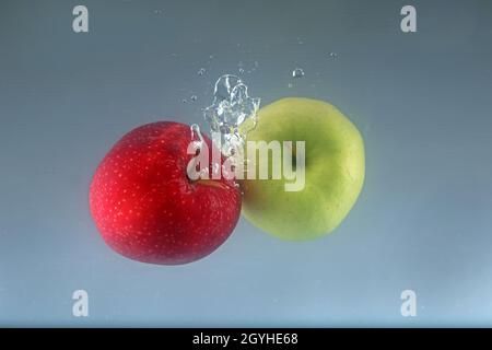 Two apples fall into water on a light background. Stock Photo