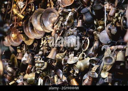 perspective view closeup of many different metallic antique pots plates and bowls of different sizes and shapes hanging on a wall in a shop Stock Photo