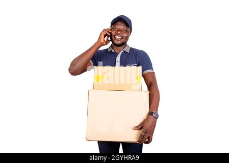 happy handsome young delivery man wearing blue uniform talking on cellphone holding two cardboard Stock Photo